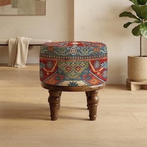 Puede incluir: Un otomán redondo y tapizado con un diseño estampado colorido en rojo, azul y dorado. El otomán se asienta sobre cuatro patas de madera oscura. La pieza es un mueble decorativo.