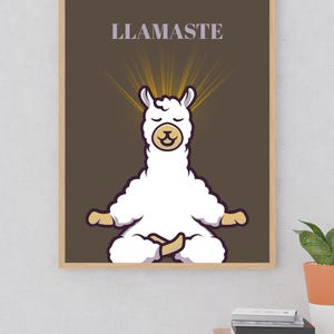 Op de afbeelding: Een ingelijste print met een cartoon lama in een yogahouding, met gouden stralen die uitstralen. Het woord "LLAMASTE" staat boven de lama. De achtergrond is bruin en de lijst is lichtbruin.