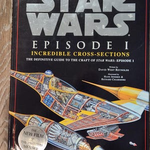 Könnte beinhalten: Ein Hardcover-Buch mit dem Titel "STAR WARS EPISODE I: Incredible Cross-Sections". Das Cover zeigt eine detaillierte Illustration eines Raumschiffs mit Querschnittsansichten, die seine inneren Komponenten zeigen. Das Buch ist ein umfassender Leitfaden für die Kunst von Star Wars: Episode 1.