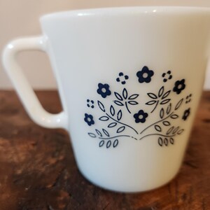 May include: White ceramic mug with a blue floral design. The design features small blue flowers and leaves.