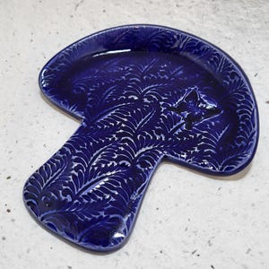 May include: A blue ceramic mushroom-shaped dish with a white floral pattern. The dish is perfect for serving snacks or holding small items.