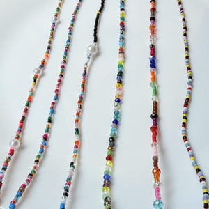 May include: A selection of beaded necklaces and eyeglass chains in various colours. The strands are made up of small, colourful beads, with larger pearl-like beads interspersed. The necklaces are displayed on a white surface.
