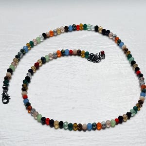 May include: A necklace made of small, colourful beads. The beads are in shades of red, orange, yellow, green, blue, and black. The necklace has a black clasp and measures approximately 40 cm in length.