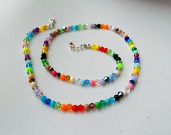 May include: A vibrant necklace composed of small, multi-coloured beads, including blue, green, yellow, orange, red, and purple. The necklace features a silver clasp and is presented on a white surface.