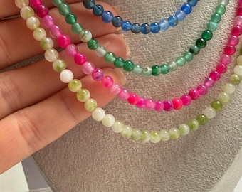 May include: A set of four layered necklaces featuring smooth, round beads in vibrant colours including blue, green, bright pink, and pale yellow. Each strand consists of uniform, polished spherical beads strung together to form a circular necklace.
