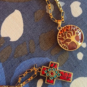 Peut inclure: Deux chaînes en or avec des pendentifs. Un pendentif est un arbre de vie rond, rouge et or. L'autre pendentif est une croix avec des mosaïques rouges, bleues et or.