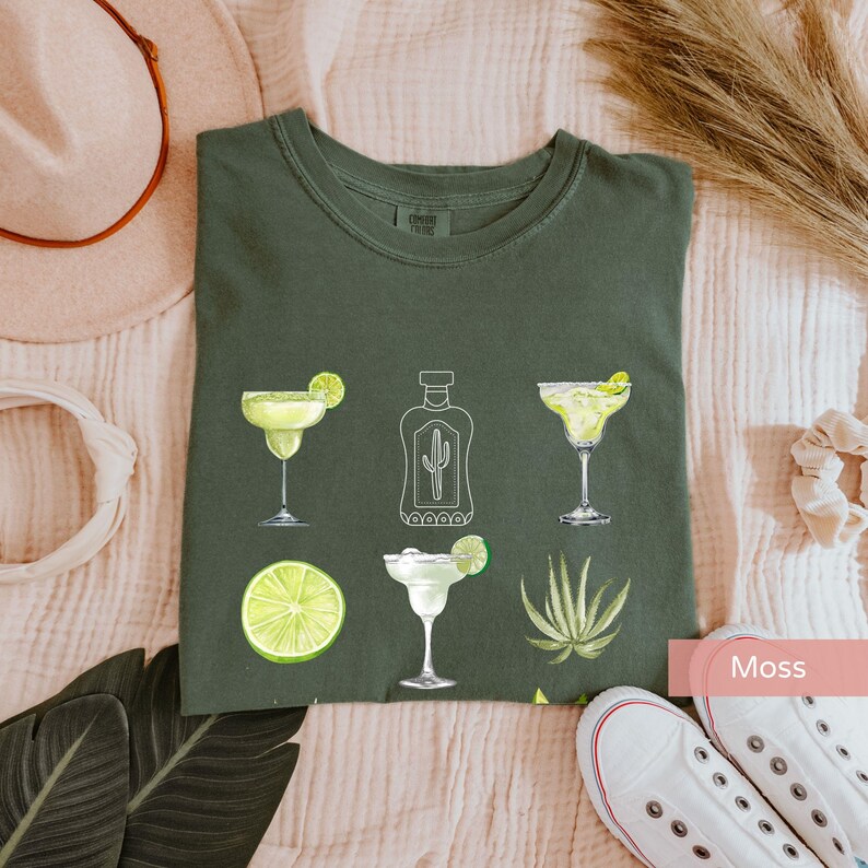May include: A green t-shirt with a white outline of a bottle of tequila, two margarita glasses, a lime, and an agave plant. The text "Moss" is visible in the lower right corner of the image.