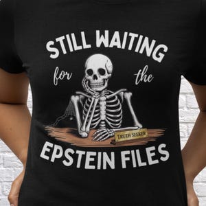 May include: Black t-shirt featuring a skeleton graphic. The skeleton is resting its chin on its hand, with the text "STILL WAITING for the EPSTEIN FILES" above and below the skeleton. A small sign reads "TRUTH SEEKER".