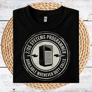 May include: Black t-shirt with a circular graphic featuring a computer server illustration and the text "Z/OS SYSTEMS PROGRAMMER AVAILABLE WHENEVER DUTY CALLS". The design is in white and gray.