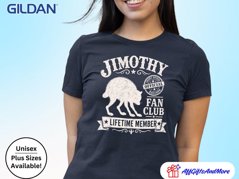 May include: A navy blue short-sleeved t-shirt featuring a white graphic of a raccoon. The text reads JIMOTHY OFFICIAL RACCOON FAN CLUB LIFETIME MEMBER. The design includes a circular badge and a banner element with a distressed, weathered texture.