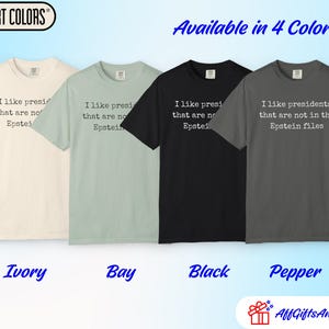 K&ouml;nnte beinhalten: Vier Comfort Colors T-Shirts in den Farben Ivory, Bay, Black und Pepper. Jedes Shirt tr&auml;gt den Text "Ich mag Pr&auml;sidenten, die nicht in den Epstein-Akten stehen." Die Shirts sind in vier Farben erh&auml;ltlich.