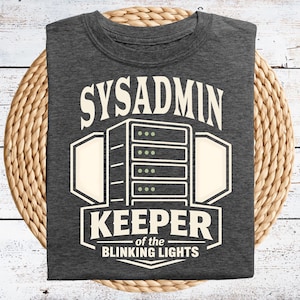 May include: Dark gray t-shirt with the text "SYSADMIN KEEPER of the BLINKING LIGHTS" in a white, stylized font. The design includes a server graphic. The shirt is displayed on a woven, circular mat.