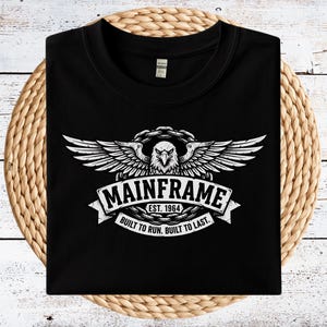 May include: Black t-shirt with a white graphic featuring an eagle with outstretched wings, a banner reading "MAINFRAME EST. 1964," and the text "BUILT TO RUN. BUILT TO LAST."