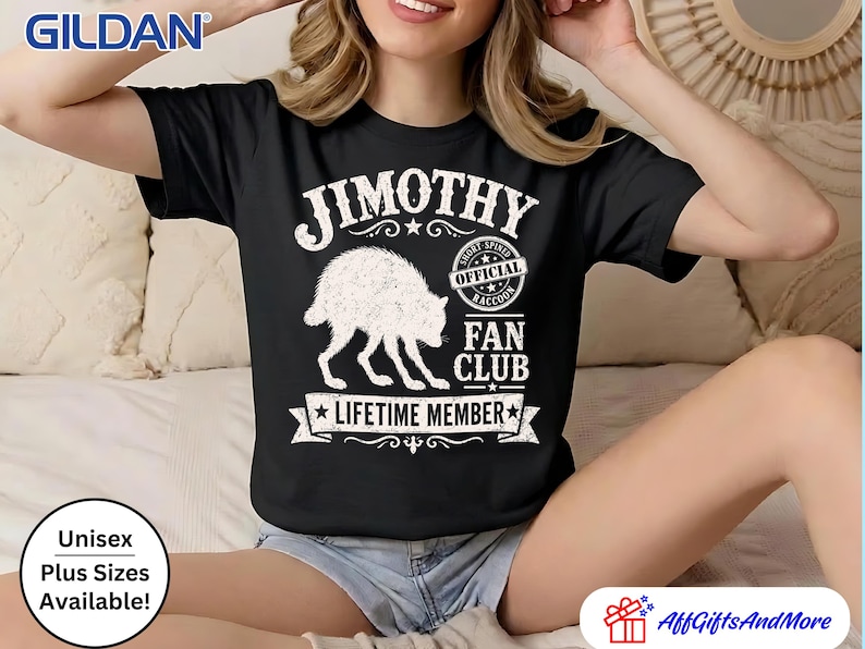 May include: A black short-sleeved t-shirt featuring a white graphic of a raccoon and text that reads JIMOTHY OFFICIAL SHORT SPINED RACCOON FAN CLUB LIFETIME MEMBER. The design includes decorative stars and banners surrounding the central animal illustration.