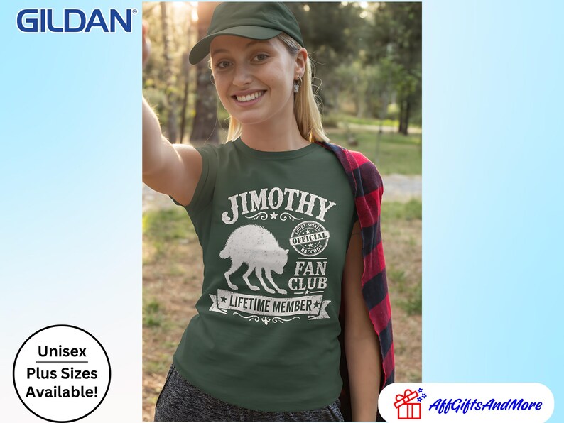 May include: A dark green short-sleeved t-shirt featuring a white graphic of a raccoon and the text JIMOTHY OFFICIAL RACCOON FAN CLUB LIFETIME MEMBER. The shirt is worn with a red and black plaid flannel shirt draped over one shoulder.
