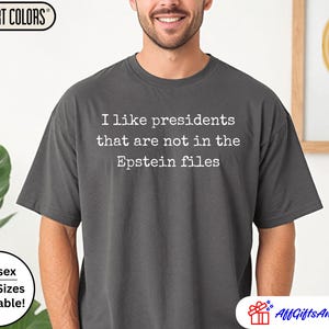 K&ouml;nnte beinhalten: Dunkelgraues Comfort Colors T-Shirt mit dem wei&szlig;en Text: "I like presidents that are not in the Epstein files". Das Shirt ist unisex und in &Uuml;bergr&ouml;&szlig;en erh&auml;ltlich.
