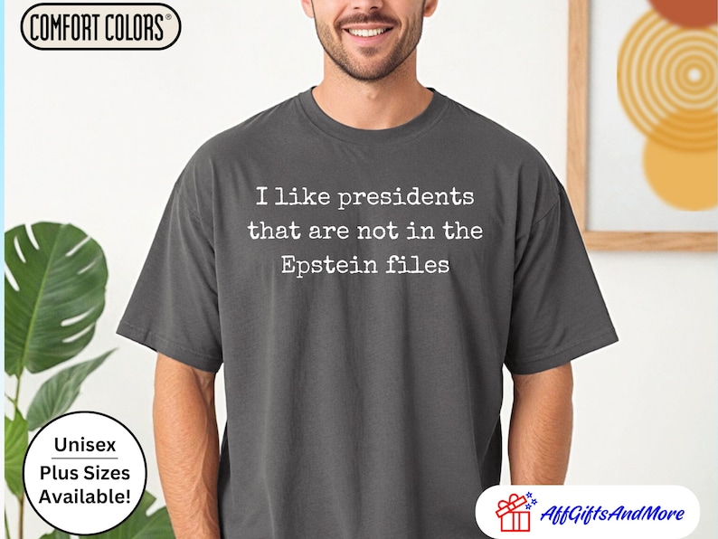 K&ouml;nnte beinhalten: Dunkelgraues Comfort Colors T-Shirt mit dem wei&szlig;en Text: "I like presidents that are not in the Epstein files". Das Shirt ist unisex und in &Uuml;bergr&ouml;&szlig;en erh&auml;ltlich.