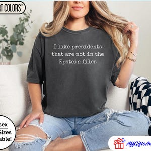 K&ouml;nnte beinhalten: Dunkelgraues Unisex-T-Shirt mit dem wei&szlig;en Text "I like presidents that are not in the Epstein files". Das Shirt ist von Comfort Colors und in &Uuml;bergr&ouml;&szlig;en erh&auml;ltlich.