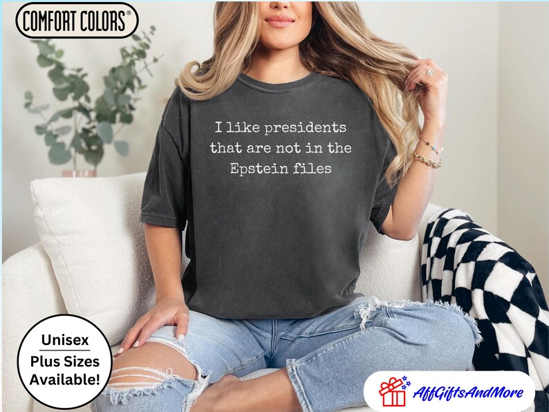 K&ouml;nnte beinhalten: Dunkelgraues Unisex-T-Shirt mit dem wei&szlig;en Text "I like presidents that are not in the Epstein files". Das Shirt ist von Comfort Colors und in &Uuml;bergr&ouml;&szlig;en erh&auml;ltlich.