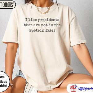 K&ouml;nnte beinhalten: Beiges Comfort Colors T-Shirt mit dem schwarzen Text "I like presidents that are not in the Epstein files". Das Shirt ist unisex und in &Uuml;bergr&ouml;&szlig;en erh&auml;ltlich.
