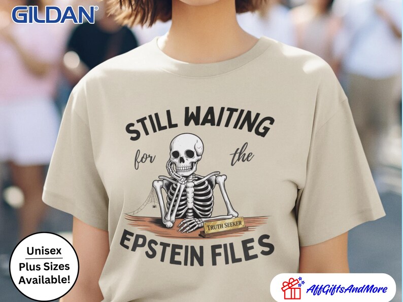 Pode incluir: Camiseta bege com o texto "STILL WAITING for the EPSTEIN FILES" e um gr&aacute;fico de esqueleto. O esqueleto est&aacute; sentado em uma mesa com uma placa de identifica&ccedil;&atilde;o "TRUTH SEEKER". A camiseta &eacute; unissex e est&aacute; dispon&iacute;vel em tamanhos grandes.