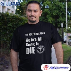 May include: Black t-shirt with the text "GOP HEALTHCARE PLAN We Are All Going to DIE" in white. The shirt features a medical symbol and is worn by a person. The Gildan logo is visible in the upper left corner.