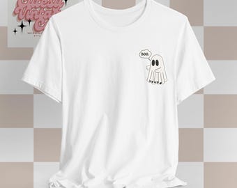 May include: White t-shirt featuring a small, black and white ghost graphic with the word "Boo." in a speech bubble. The shirt has a classic crew neck and short sleeves. The design is simple and suitable for Halloween or everyday wear.