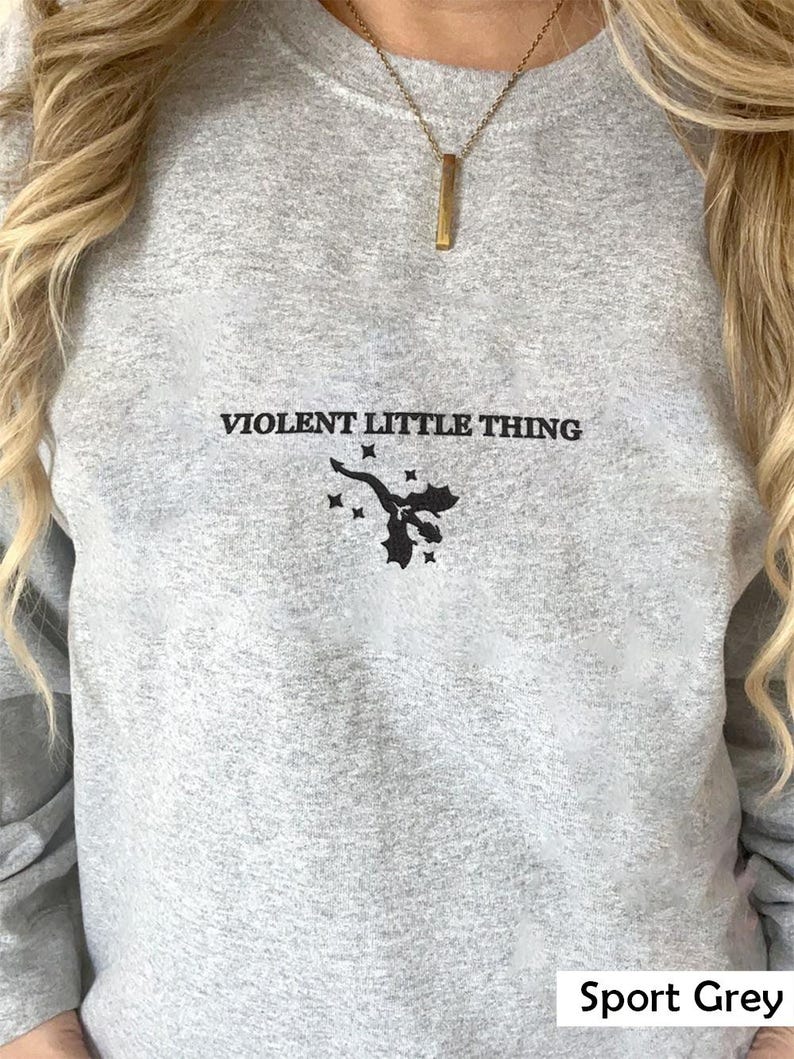 Puede incluir: Una sudadera gris jaspeada con el texto "VIOLENT LITTLE THING" y un peque&ntilde;o gr&aacute;fico negro de un drag&oacute;n. La sudadera tiene un corte holgado y cuello redondo.