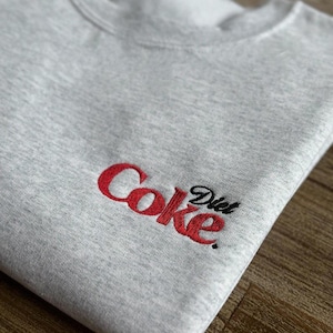 May include: Gray sweatshirt with a red embroidered logo that says "Diet Coke" in a stylized font.