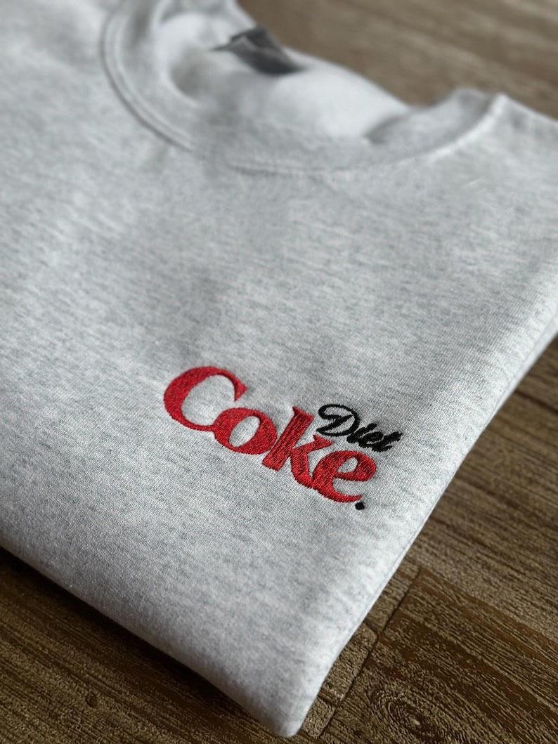 May include: Gray sweatshirt with a red embroidered logo that says "Diet Coke" in a stylized font.