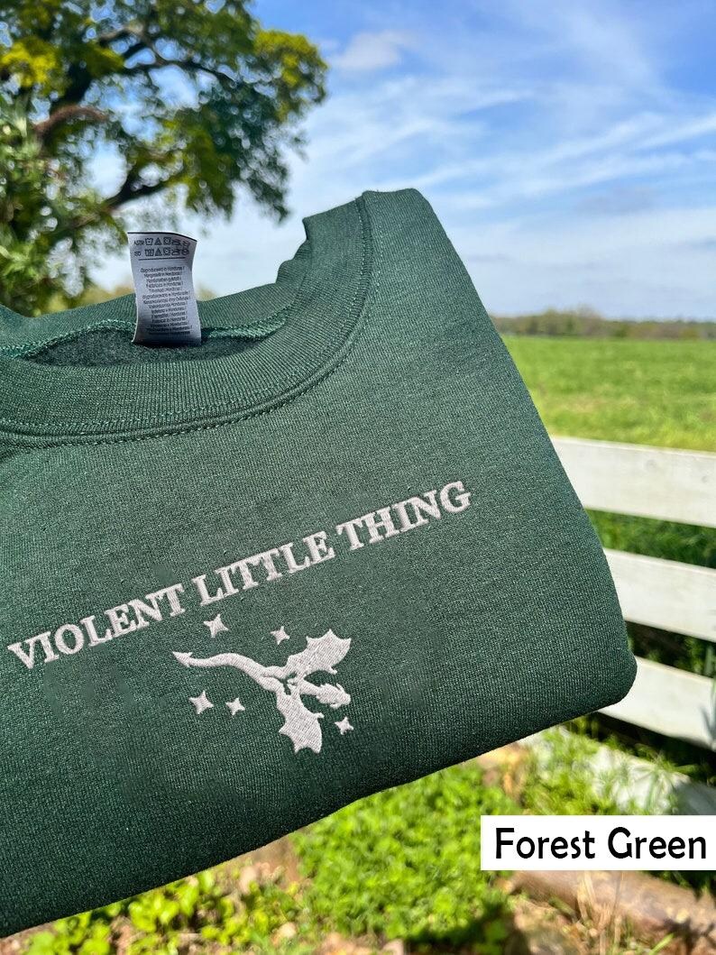 Puede incluir: Sudadera verde bosque con el texto "VIOLENT LITTLE THING" y un dise&ntilde;o de drag&oacute;n bordado en blanco.