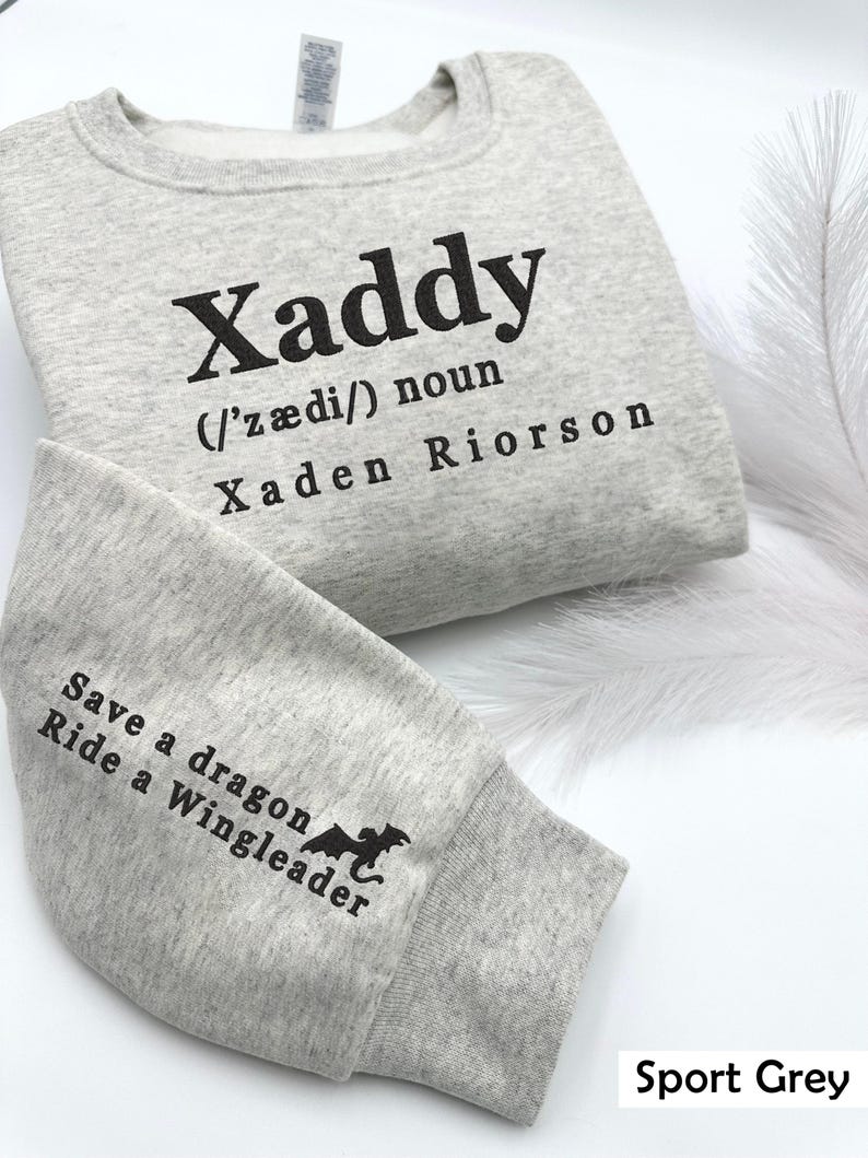 May include: A gray sweatshirt with the text "Xaddy (/ˈz&aelig;di/) noun Xaden Riorson" on the front and "Save a dragon Ride a Wingleader" on the sleeve. The sweatshirt is labeled "Sport Grey".