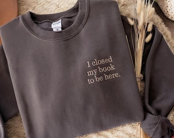 May include: A dark gray sweatshirt with the text "I closed my book to be here." embroidered on the front.