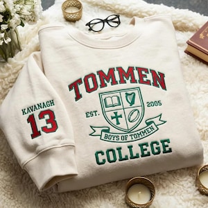 May include: Cream-colored sweatshirt with the word "TOMMEN" in red and green lettering. The sweatshirt features a crest with a book, harp, cross, and football. The sleeve displays "KAVANAGH 13". The text "BOYS OF TOMMEN COLLEGE" is also visible.