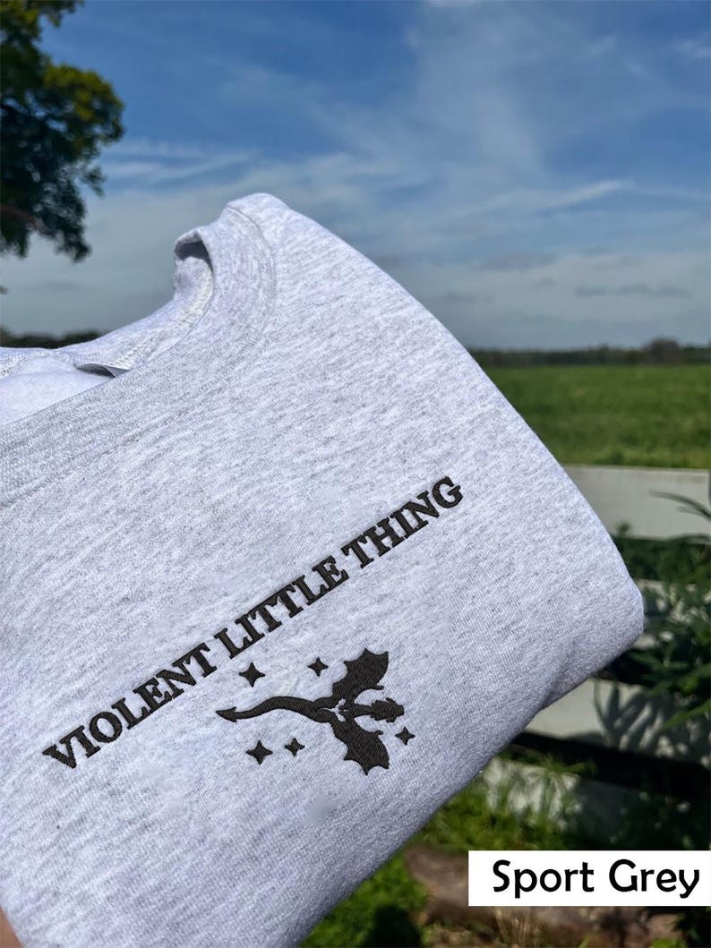 Puede incluir: Una sudadera gris con el texto "VIOLENT LITTLE THING" impreso en la parte delantera. La sudadera tambi&eacute;n presenta un peque&ntilde;o gr&aacute;fico negro de un drag&oacute;n con estrellas.