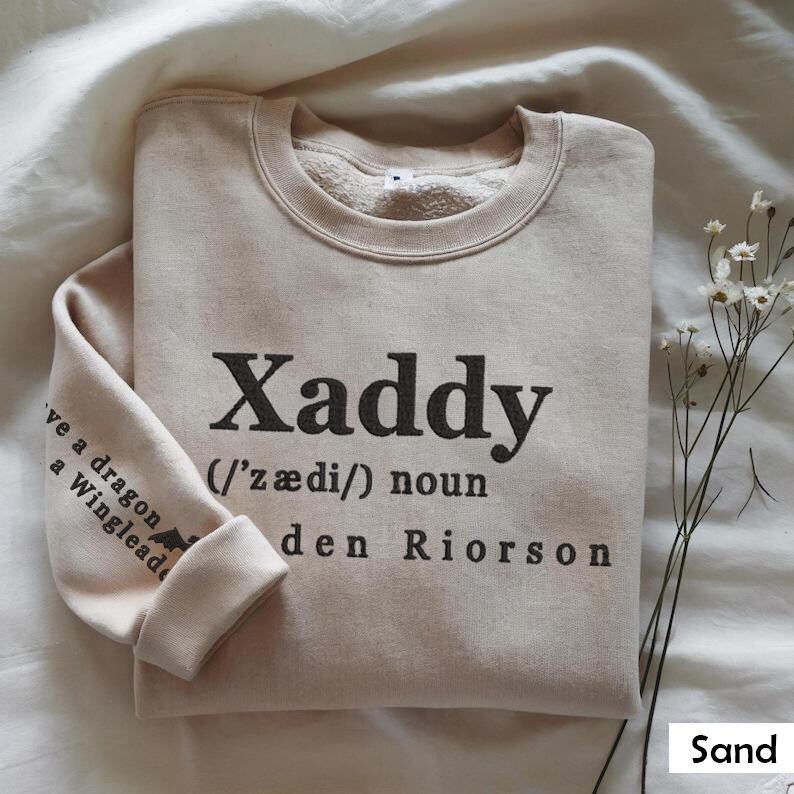 May include: A beige sweatshirt with the word "Xaddy" printed on the front, defined as a noun and pronounced as "/'z&aelig;di/" with the name "den Riorson" printed below. The sweatshirt has a fleece lining.