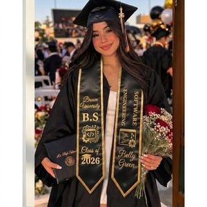 May include: A person in a black graduation gown and cap, holding a diploma and a bouquet of red roses. The sash reads "Brown University B.S. Software Engineering Class of 2026 Belly Green."