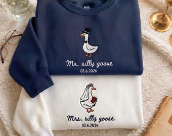 May include: A navy blue sweatshirt featuring an embroidered goose in a top hat and bowtie with the text Mr. silly goose 03.6.2026, layered over a white sweatshirt with an embroidered goose in a veil and flowers with Mrs. silly goose 03.6.2026.