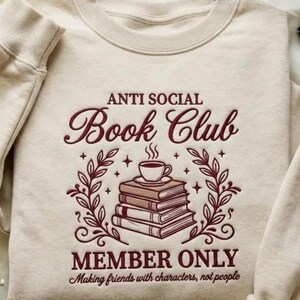 May include: A cream-coloured sweatshirt featuring the burgundy text "ANTI SOCIAL Book Club". An illustration of books and a coffee cup is below the text, with the words "MEMBER ONLY" beneath. The sweatshirt has a crew neck and long sleeves.