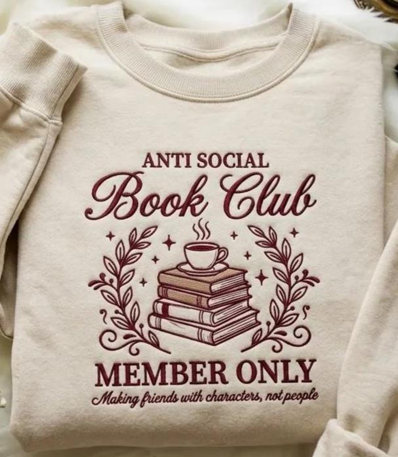 May include: A cream-coloured sweatshirt featuring the burgundy text "ANTI SOCIAL Book Club". An illustration of books and a coffee cup is below the text, with the words "MEMBER ONLY" beneath. The sweatshirt has a crew neck and long sleeves.