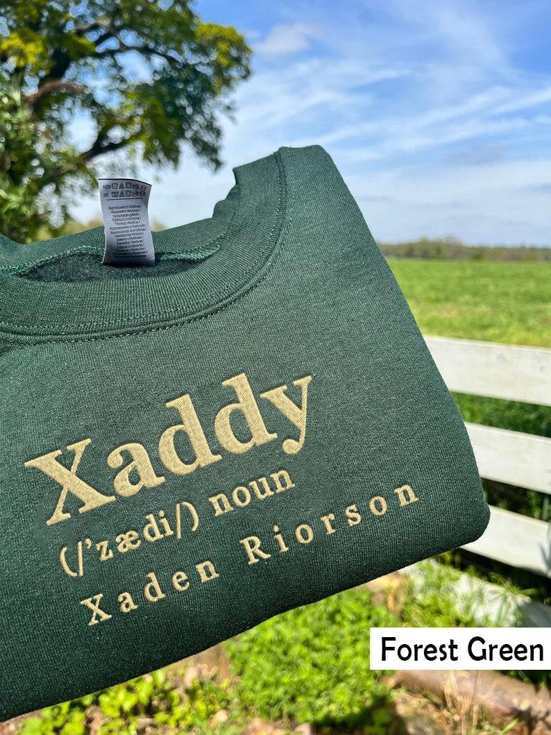 May include: Forest green sweatshirt with the word "Xaddy" in gold embroidery. The word is defined as a noun and the name "Xaden Riorson" is written below it.