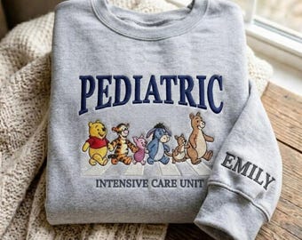 Bluza z haftem dla pielęgniarki oddziału intensywnej terapii pediatrycznej, okrągły dekolt z postaciami Kubusia Puchatka, spersonalizowany rękaw z imieniem, uroczy prezent dla pielęgniarki pediatrycznej