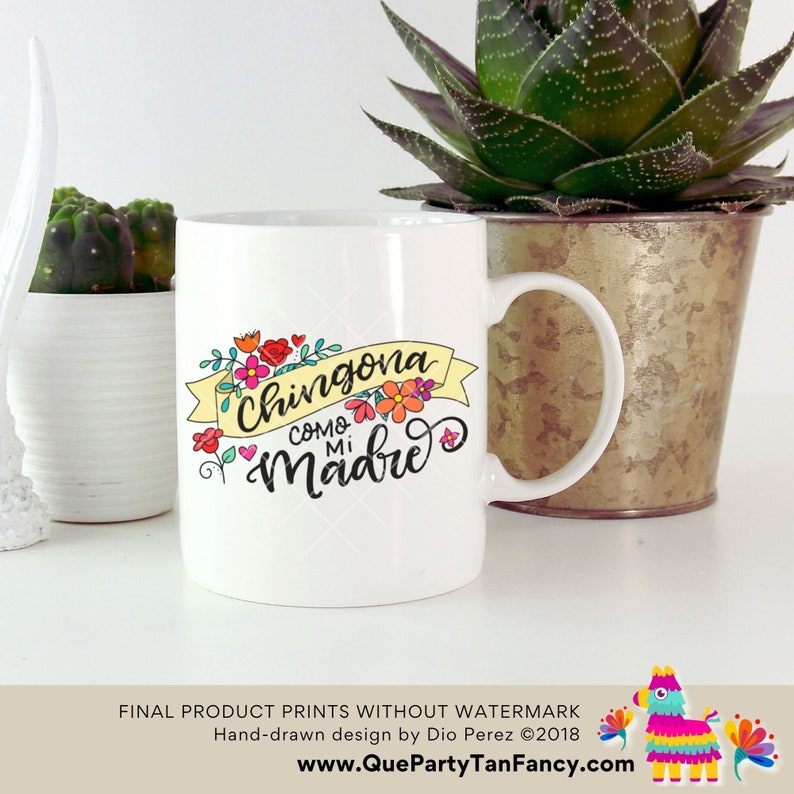 May include: White ceramic mug with a colorful floral design and the text "Chingona como mi madre" in black script. The mug has a handle and is sitting on a white surface.