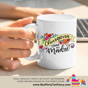 May include: White ceramic coffee mug with a colorful graphic design featuring the text "Chingona Como Mi Madre" in a whimsical font. The design includes flowers and hearts.