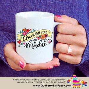 May include: White ceramic mug with a yellow banner that reads "Chingona como mi Madre" in black lettering. The banner is decorated with colorful flowers and hearts.