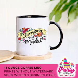May include: White ceramic coffee mug with a black rim and handle. The mug features a colorful graphic with the text "Chingona Como Mi Madre" in black lettering with a yellow banner and floral accents.