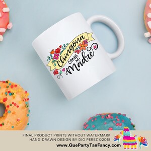 May include: White ceramic mug with a yellow banner that says "Chingona como mi Madre" in black script. The banner is decorated with colorful flowers.