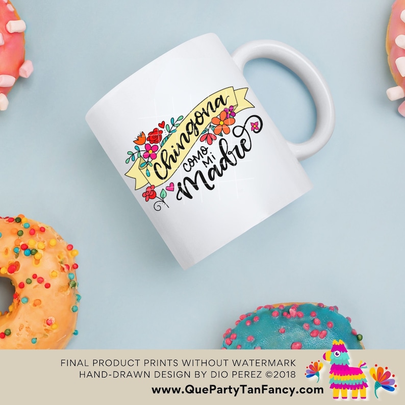 May include: White ceramic mug with a yellow banner that says "Chingona como mi Madre" in black script. The banner is decorated with colorful flowers.