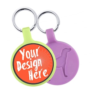 Puede incluir: Dos llaveros redondos con anillos plateados. Uno es verde lima con un centro naranja y el texto "Your Design Here". El otro es morado con una silueta de perro.