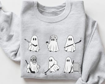 May include: A light gray crewneck sweatshirt featuring a black and white graphic print of six ghosts playing ice hockey. The ghosts are depicted in various poses, including holding hockey sticks, wearing goalie masks, and standing near a hockey net.